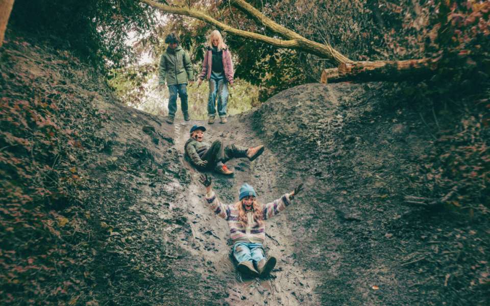 Four people on a steep, muddy forest slope surrounded by trees and dense vegetation.