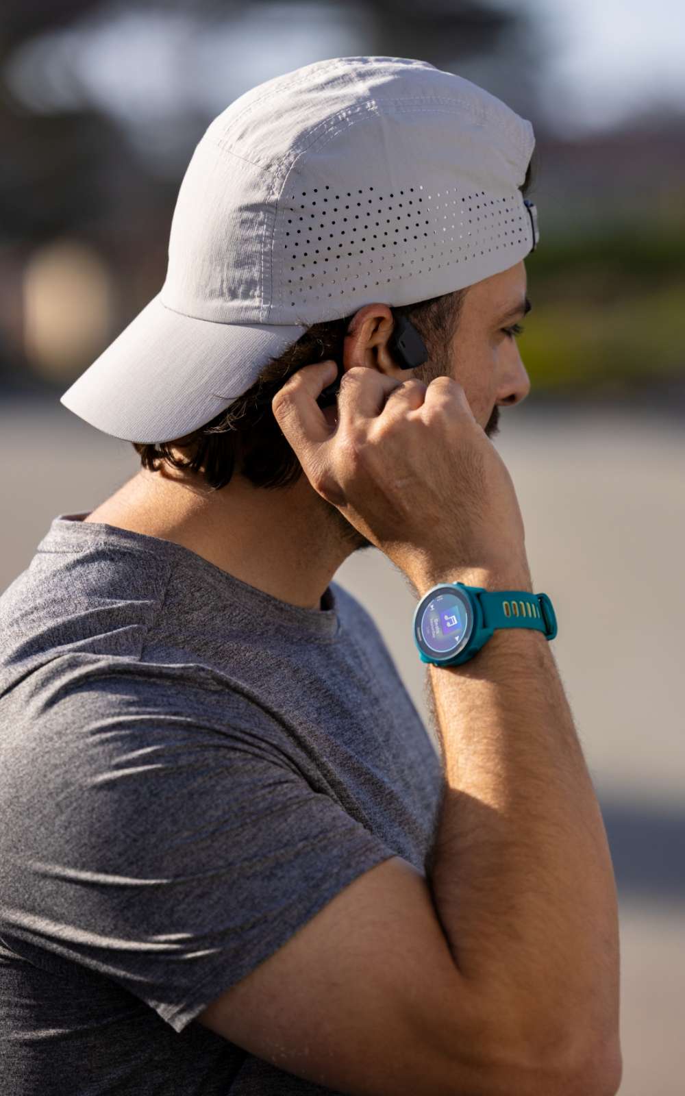 Personne avec casquette blanche mettant un écouteur et portant une montre de sport.