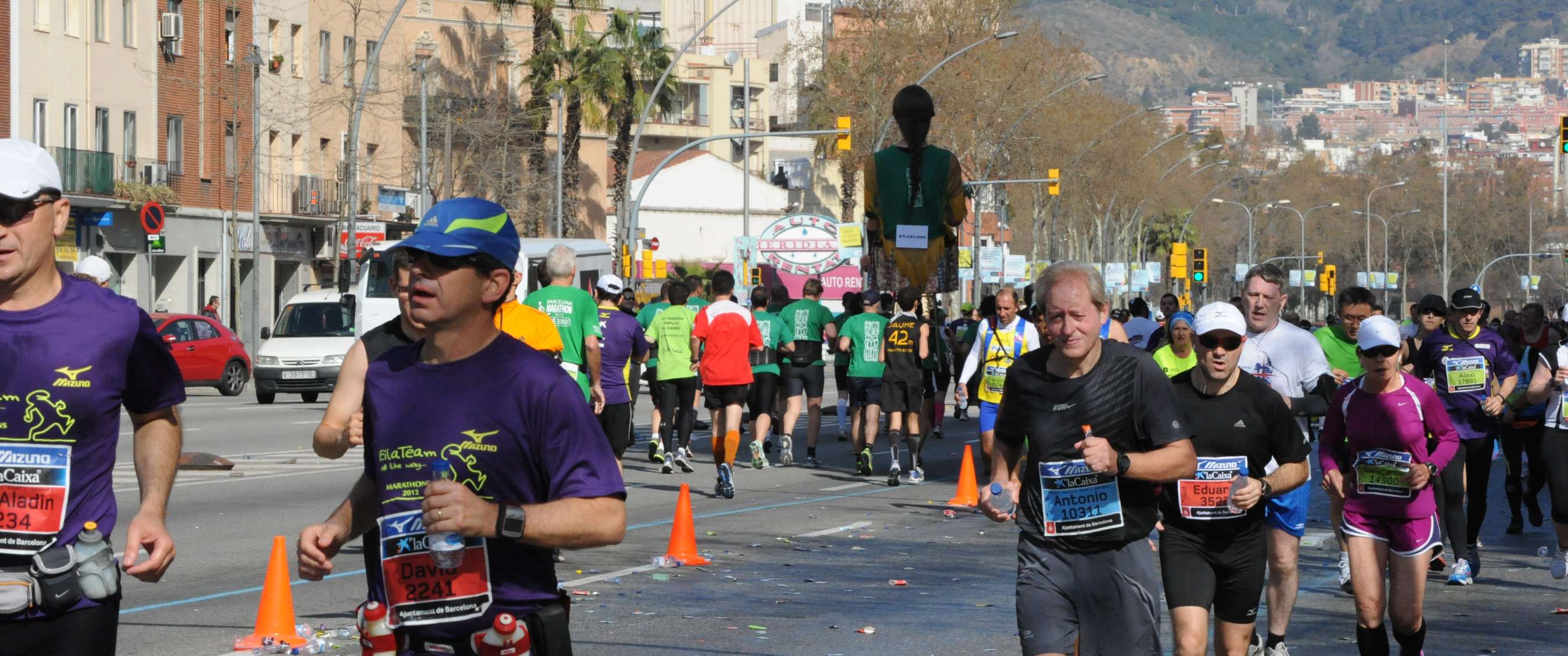 Groupe de coureurs lors d’un marathon urbain à Barcelone, avec des immeubles, des palmiers et des collines en arrière-plan