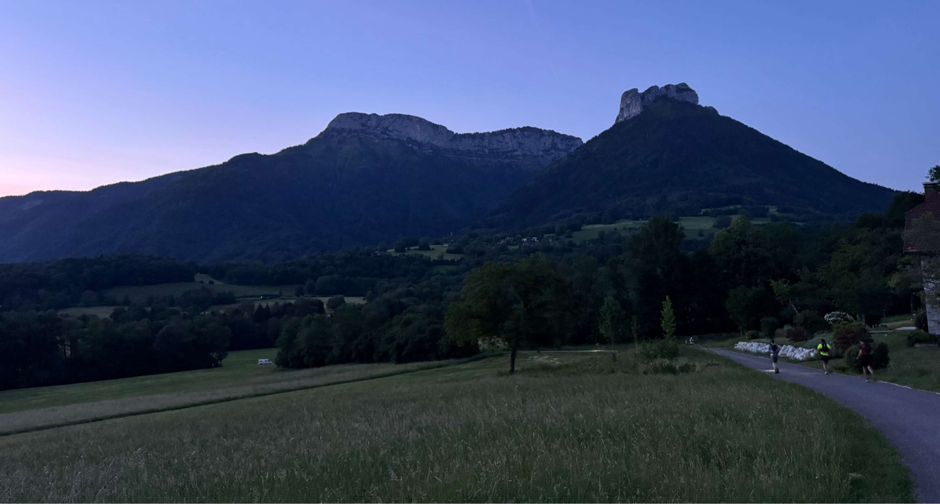 Trois coureurs avancent sur une route dans un paysage montagneux au crépuscule.