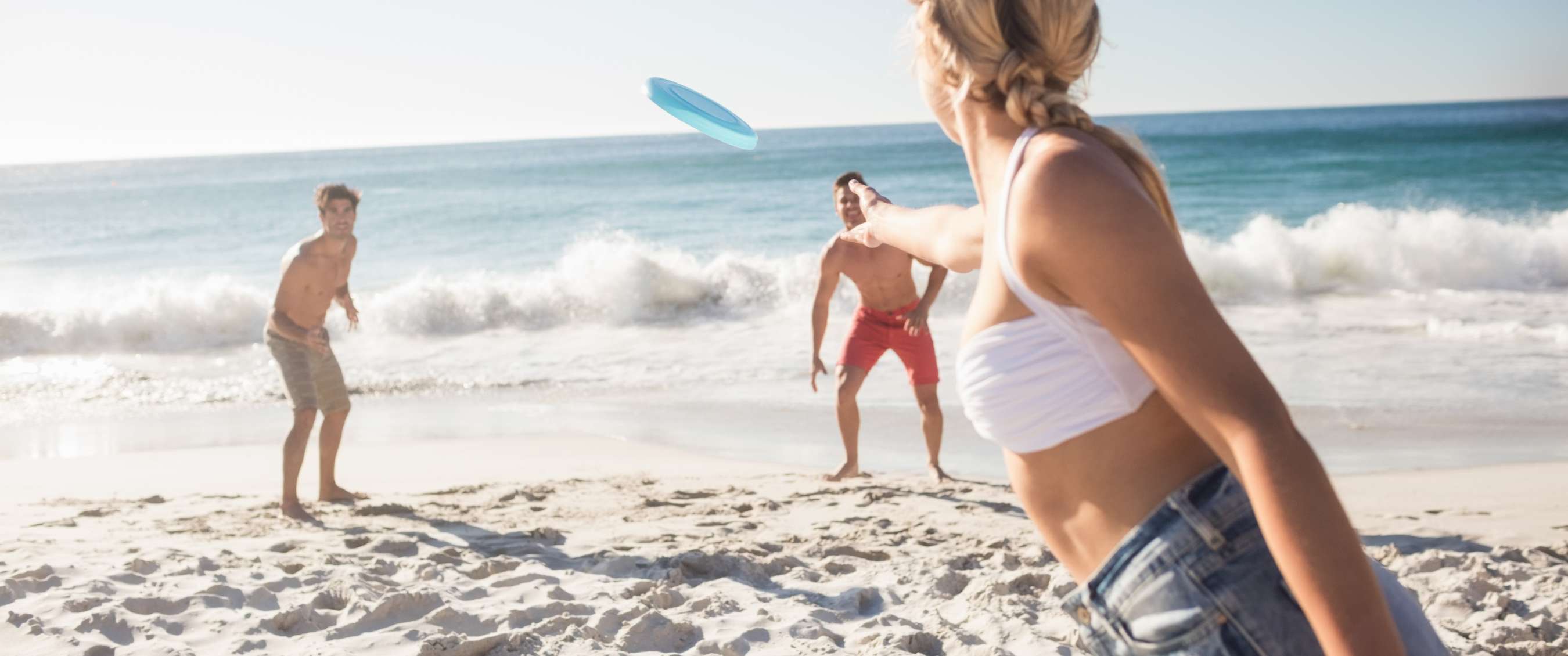Trois personnes jouent avec un frisbee bleu sur la plage, près des vagues.