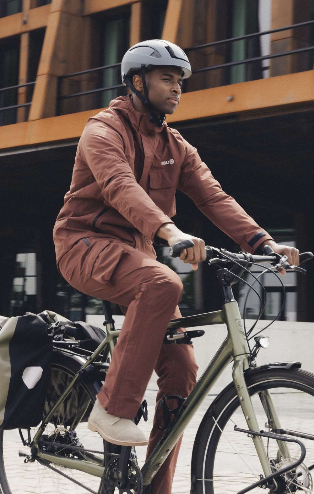 Man fietst door de stad met een witte fietshelm en bruine regenoutfit