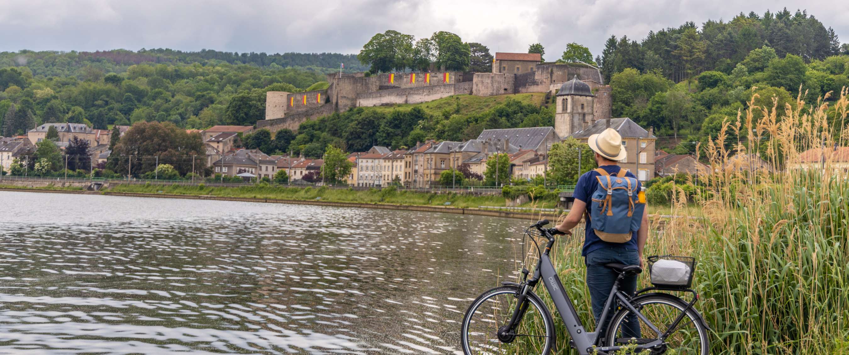 Fietser met fiets aan de rivier, met uitzicht op een vestingstad op een heuvel.
