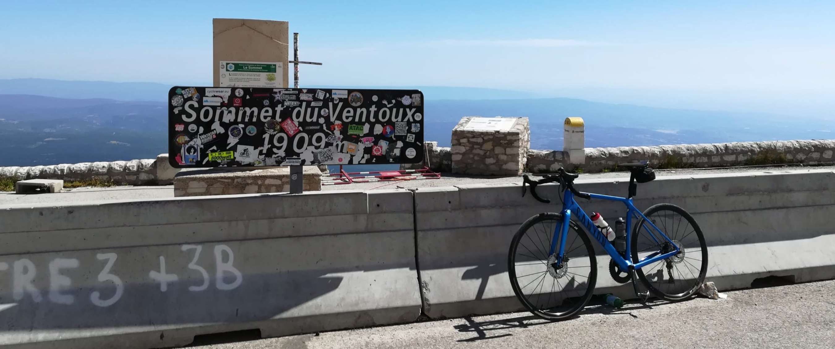 Vélo de route bleu à côté du panneau « Sommet du Ventoux 1909 m » au sommet.