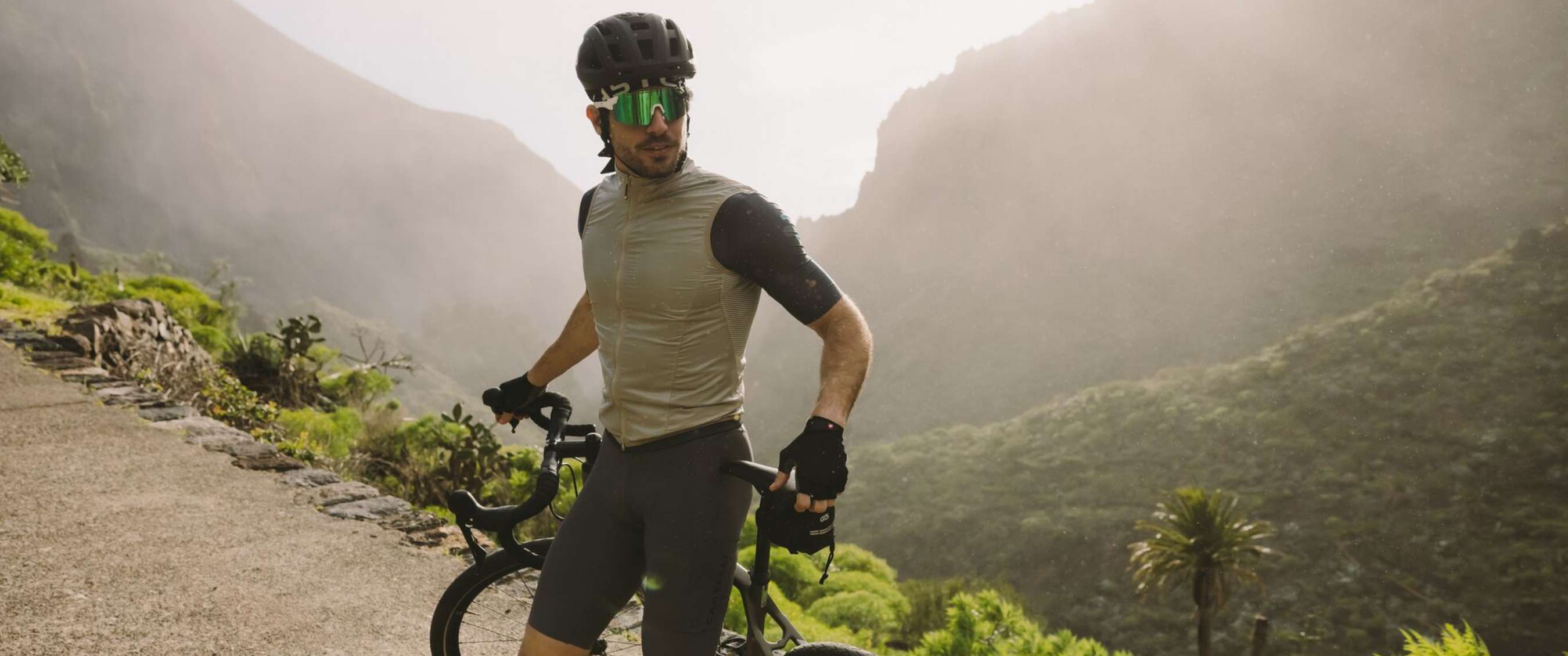 Cycliste avec casque et lunettes à côté d’un vélo de route en montagne.
