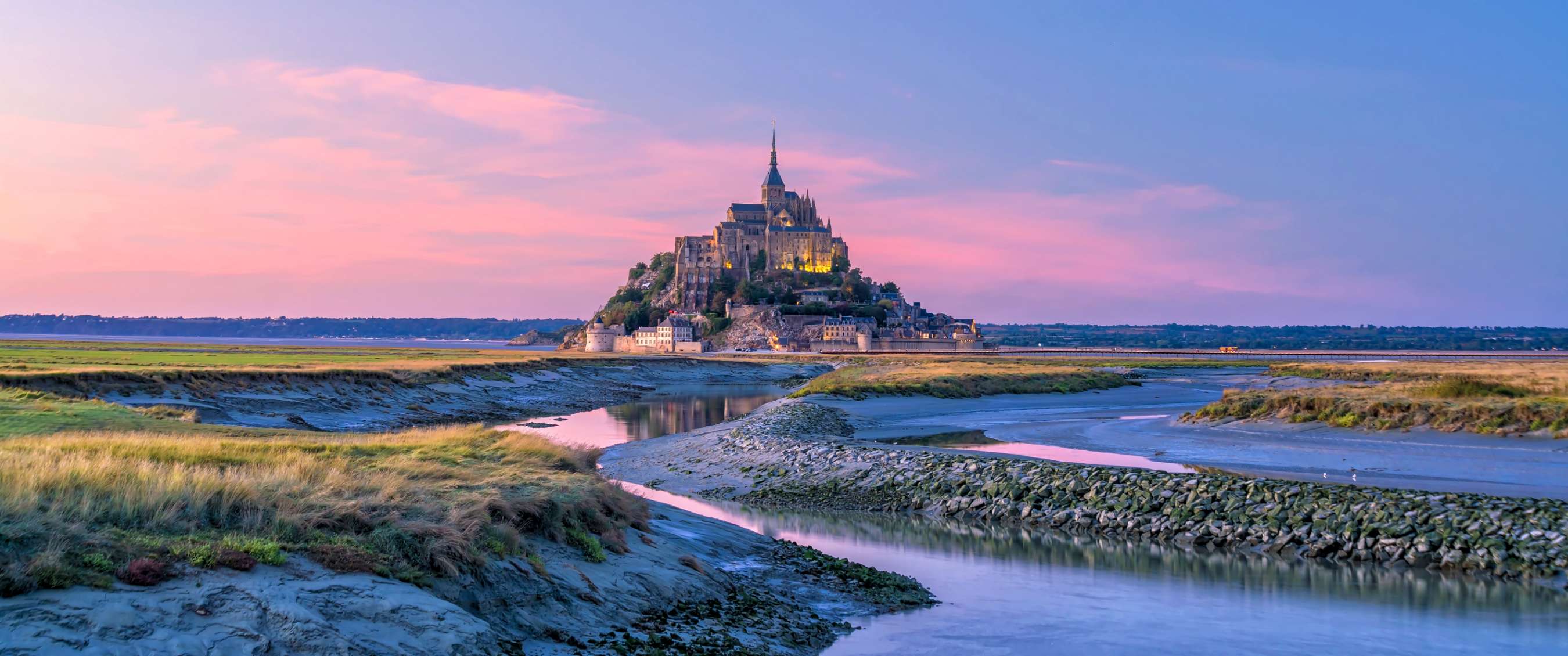 Mont-Saint-Michel au coucher du soleil, avec eau et vasières au premier plan