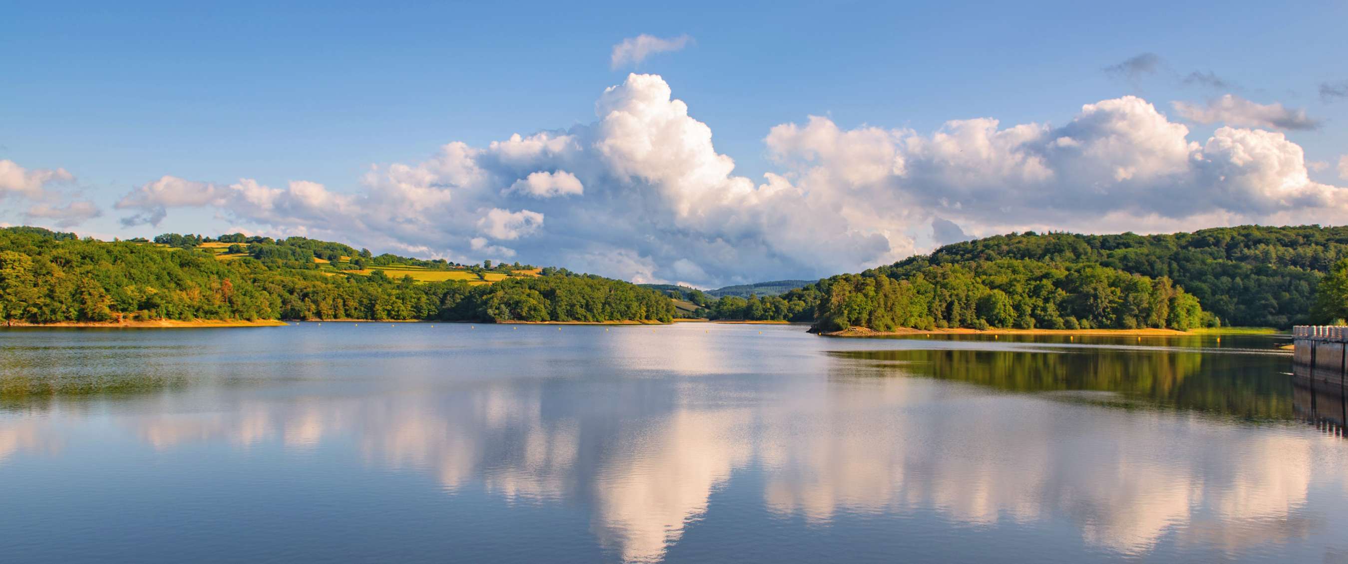 Lac avec reflet des nuages et rives boisées sous un ciel bleu