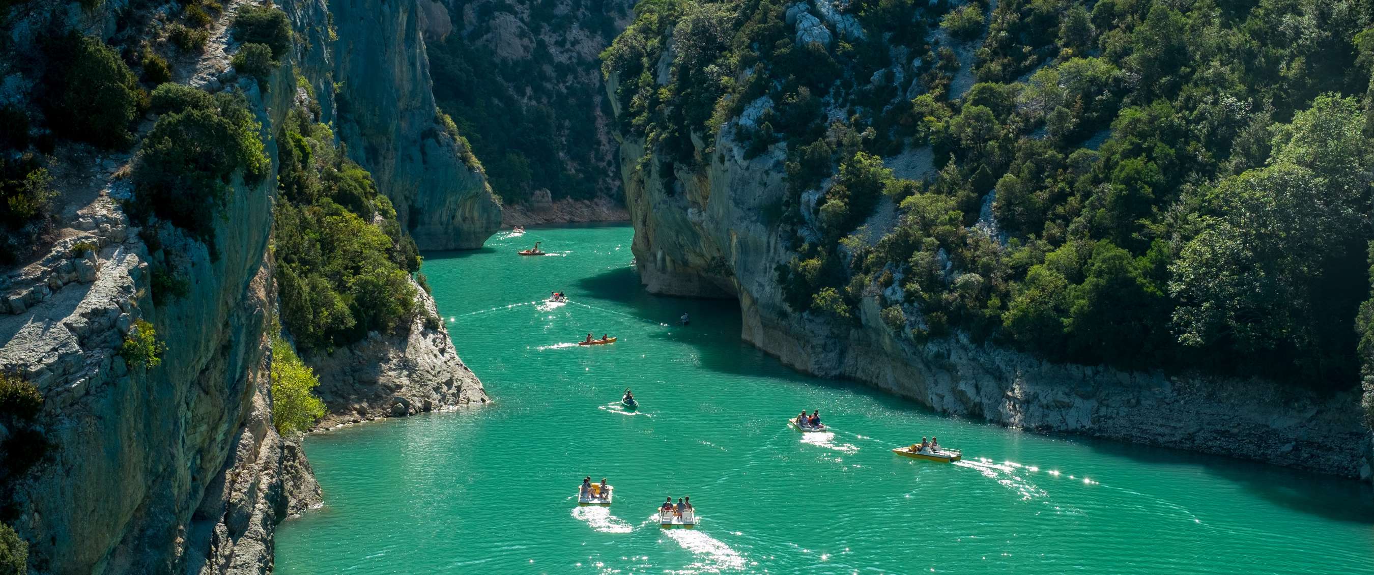 Gorge aux parois rocheuses abruptes avec plusieurs bateaux sur une eau vert bleu clair