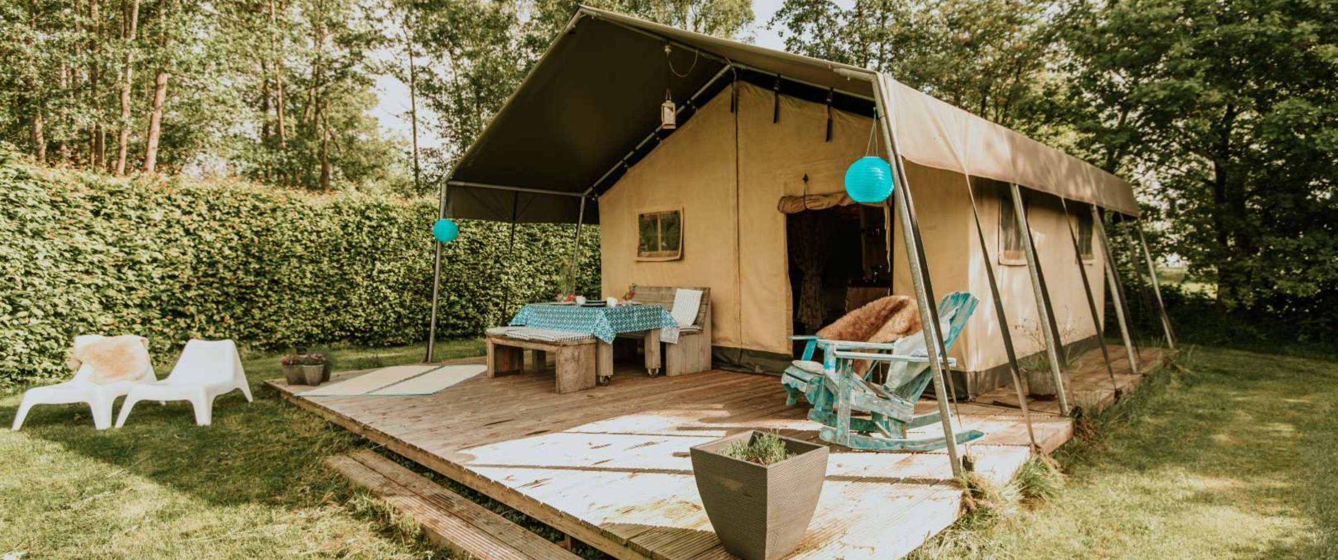 Tente safari avec terrasse en bois, table, chaises et lanternes bleues