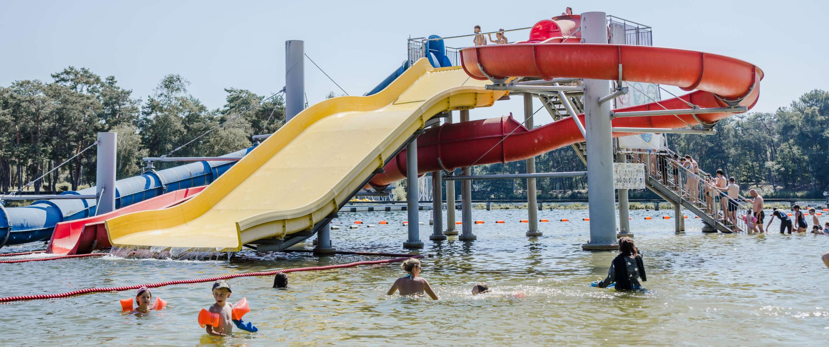 Grote waterglijbanen boven een zwemgedeelte waar verschillende personen in het water spelen.