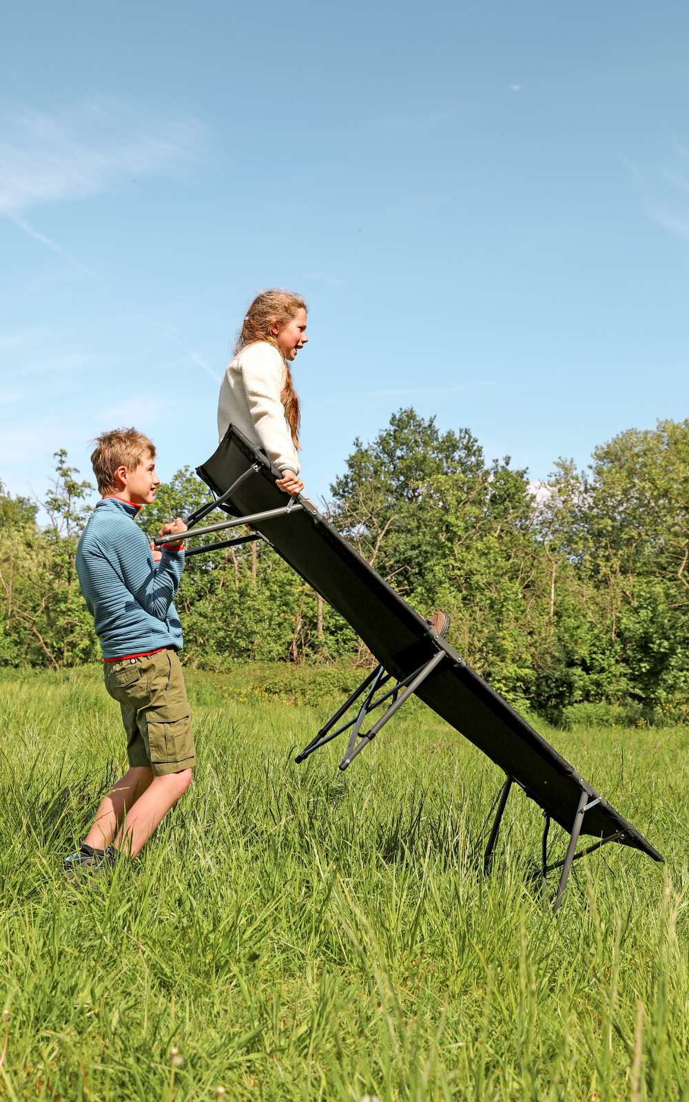 Des enfants jouent avec un lit de camp dans un champ ensoleillé.