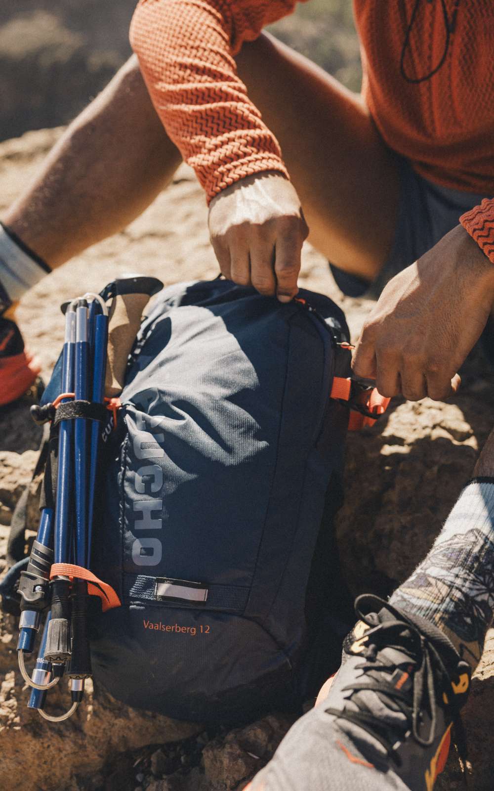 Handen sluiten een donkere rugzak met wandelstokken aan de zijkant.