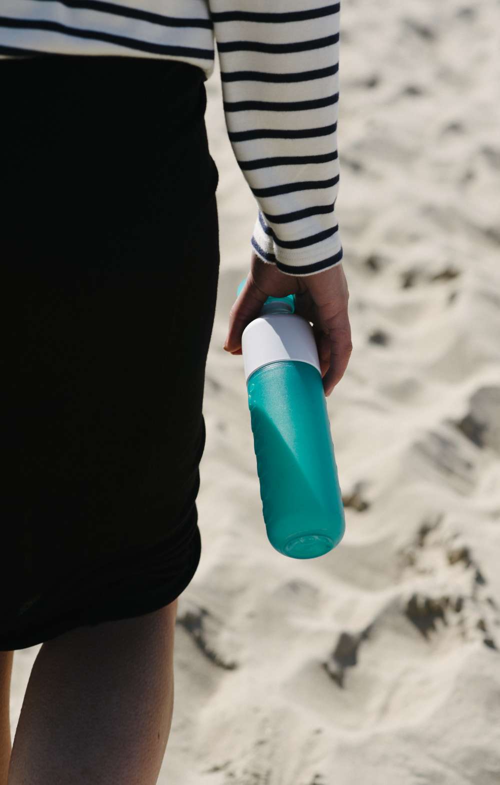 Gros plan sur une gourde turquoise tenue à la main sur la plage