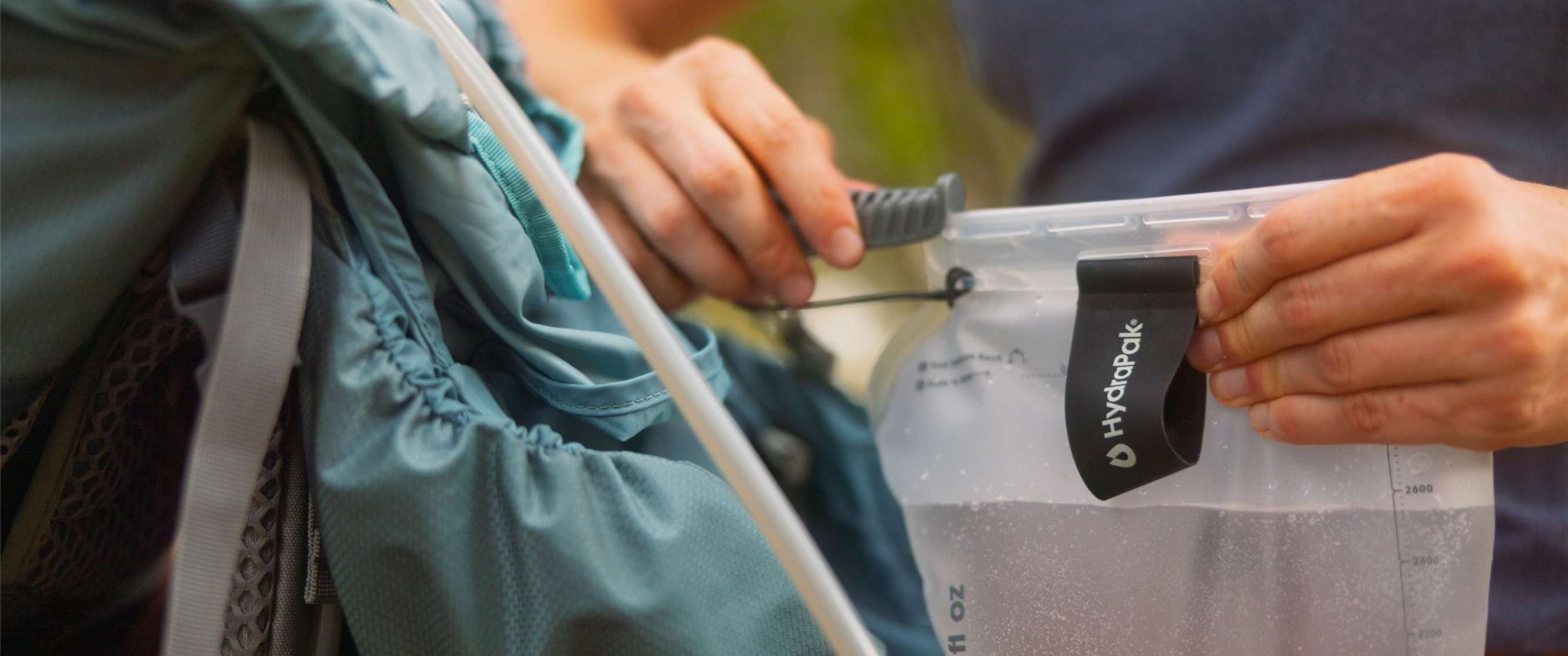 Handen vullen een HydraPak-waterzak in een rugzak met een drinkslang zichtbaar.