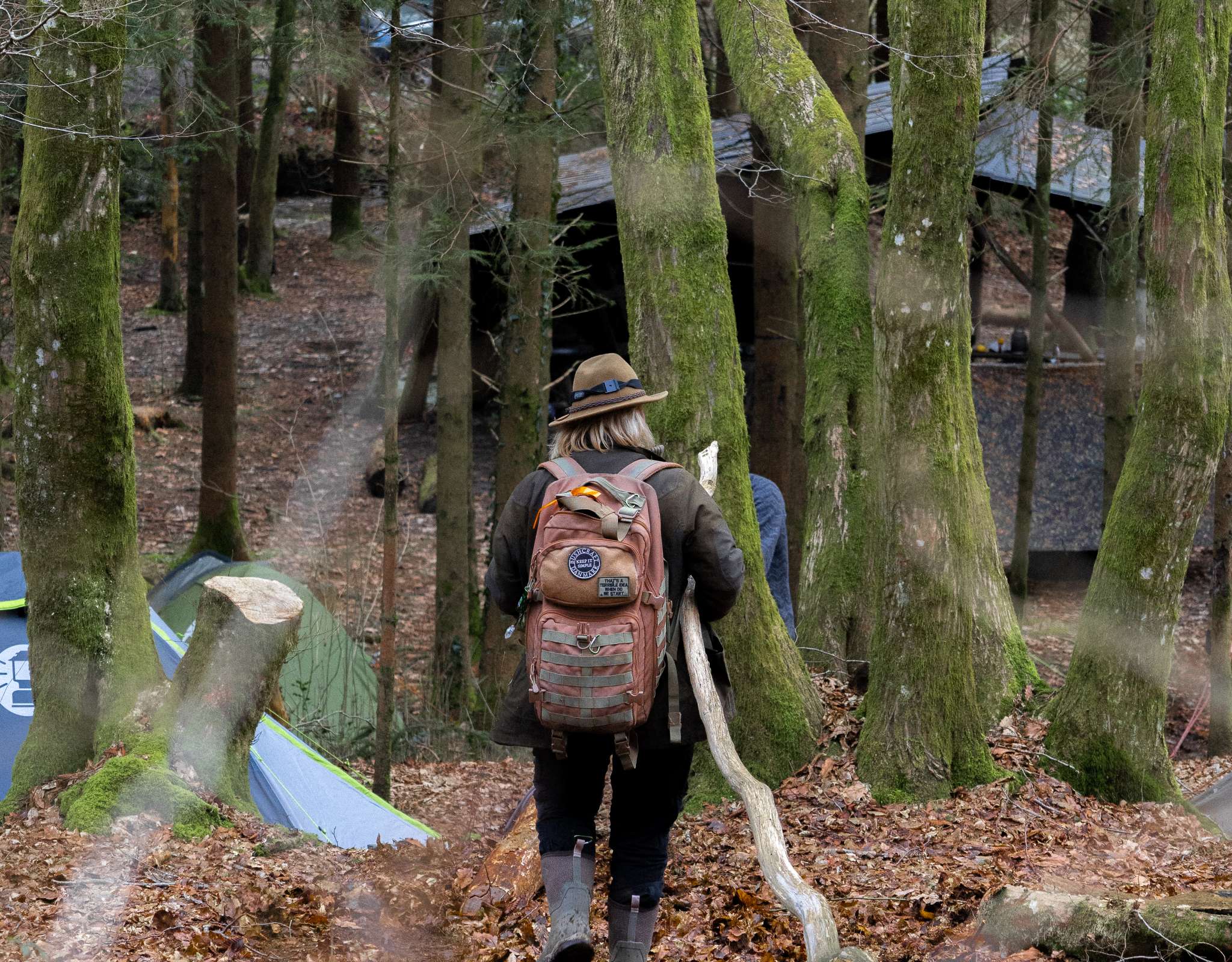 Randonneur avec sac à dos marchant dans un camping forestier avec des tentes.