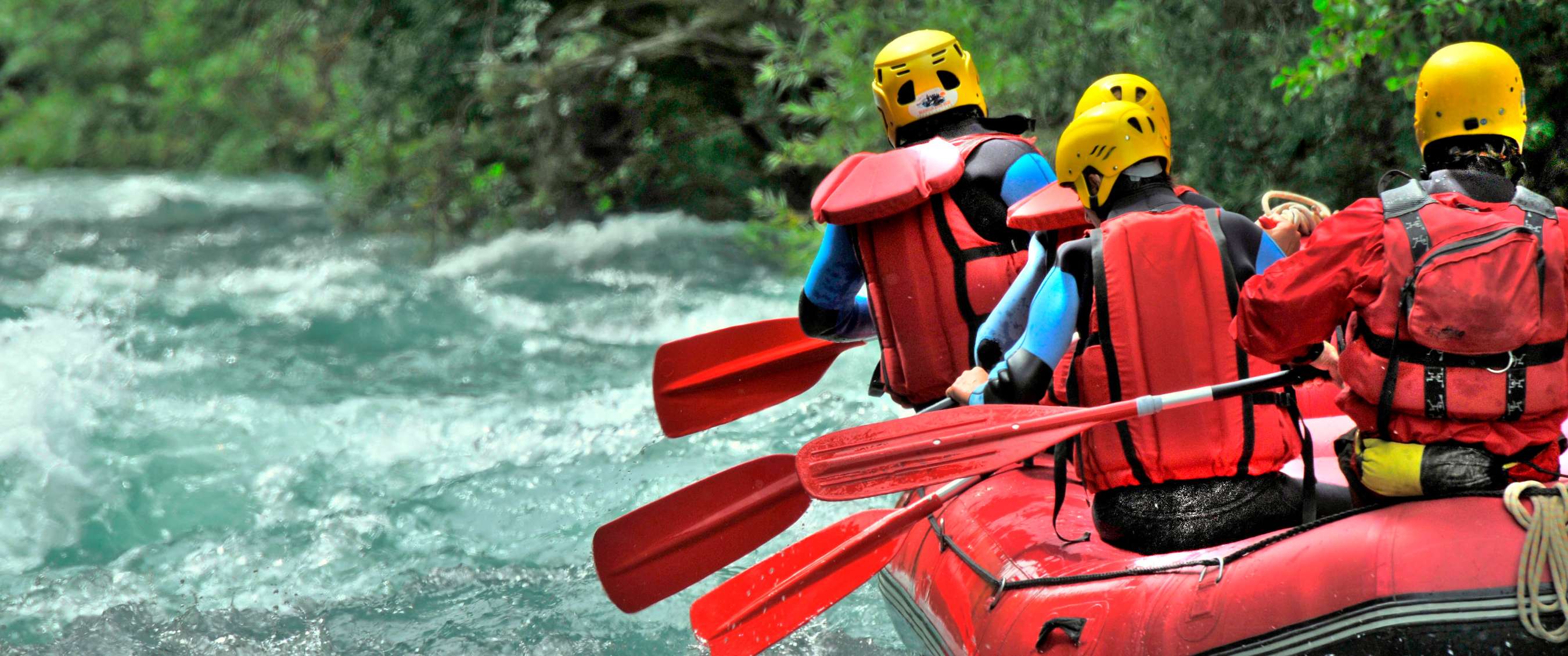 Un groupe de rafteurs pagaye dans un bateau rouge sur une rivière agitée bordée de verdure.