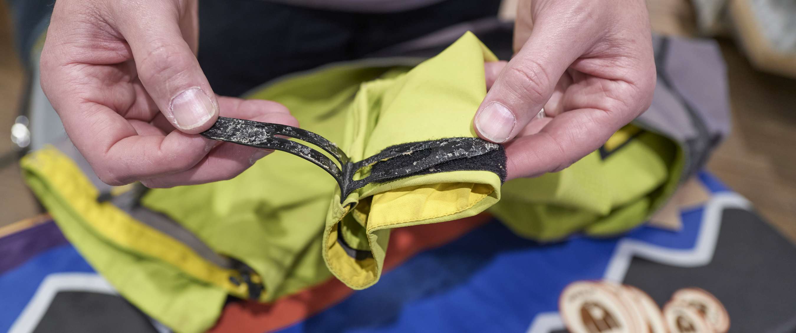 Close-up van handen die een versleten lus aan een groen kledingstuk vasthouden.