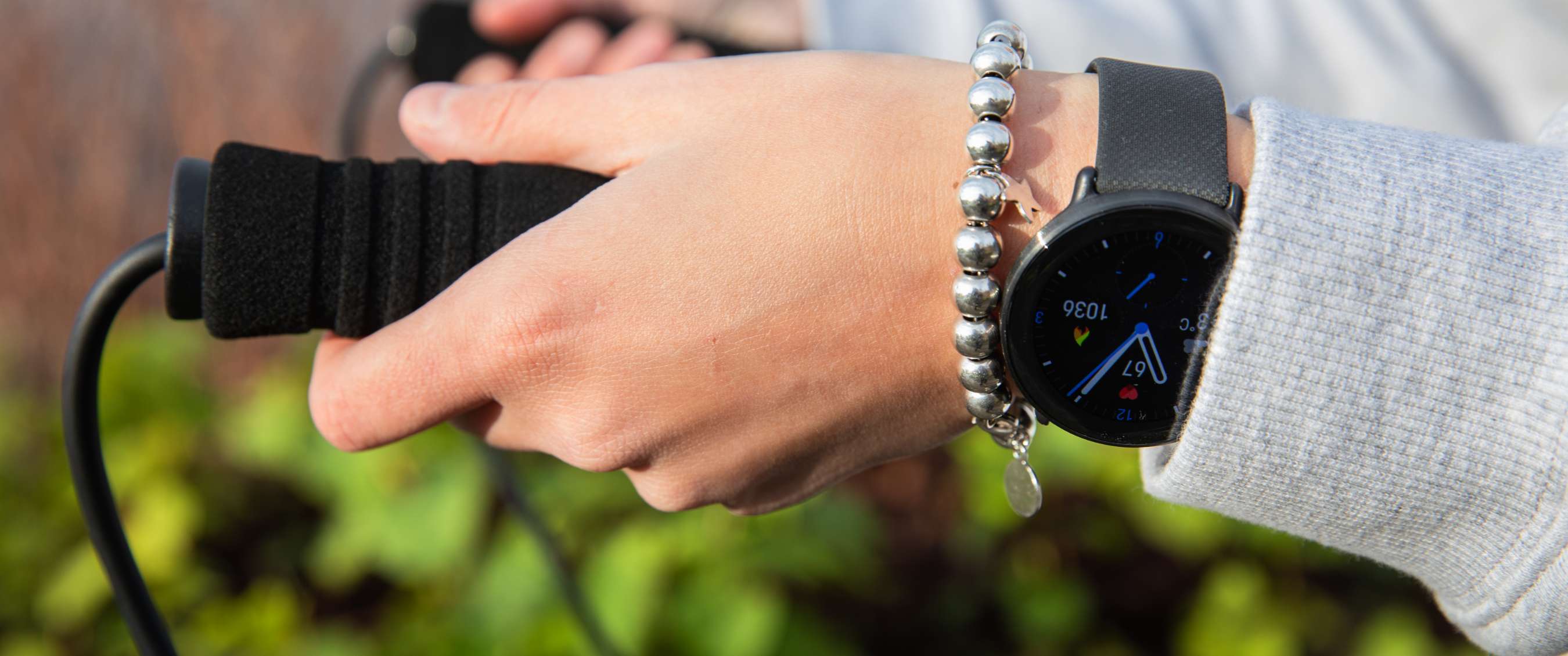 Hand met zwarte smartwatch en zilveren kralenarmband houdt buiten een zwart handvat vast.