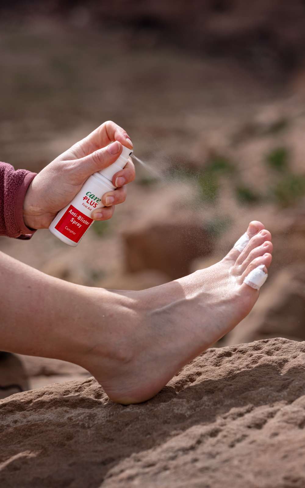 Care Plus Anti-Blister Spray est appliqué sur un pied avec un orteil bandé.