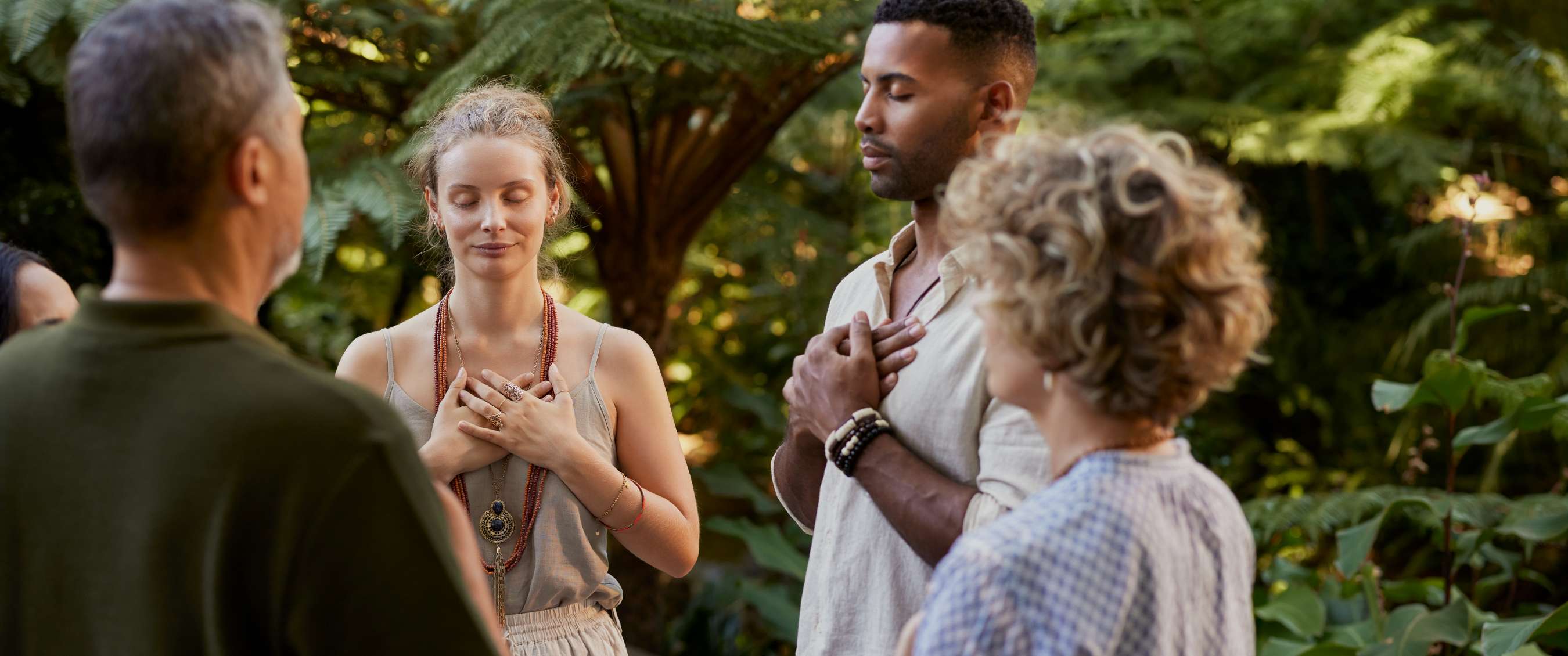 Groep mensen die met gesloten ogen mediteert in een groene buitenomgeving.