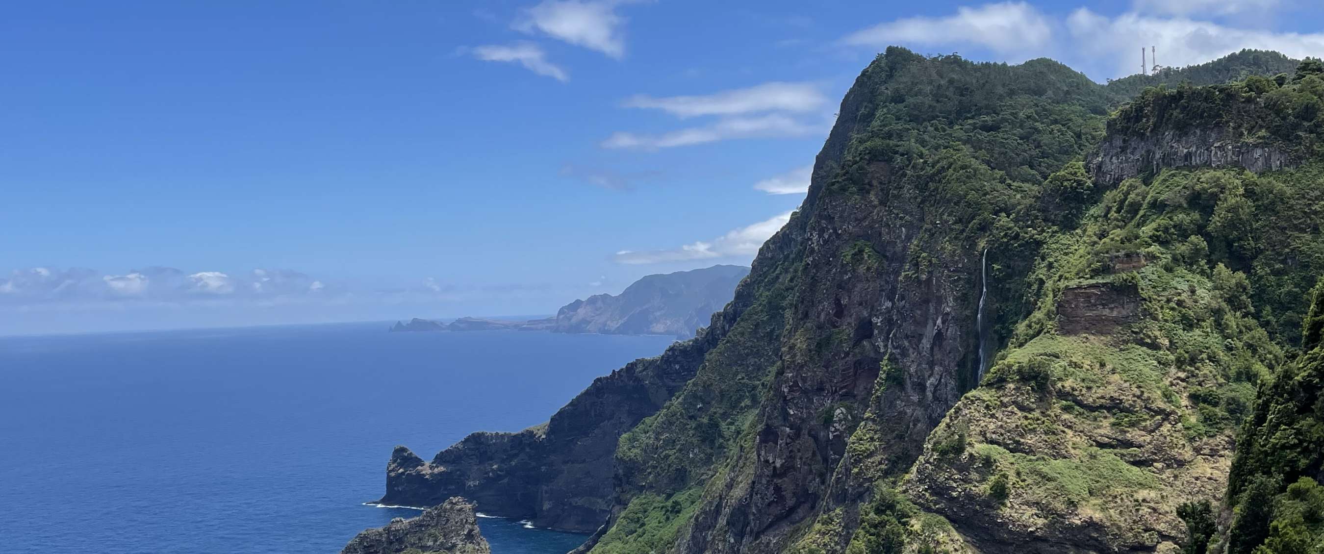 Rotsachtige kust met begroeide bergen, oceaan en helderblauwe lucht