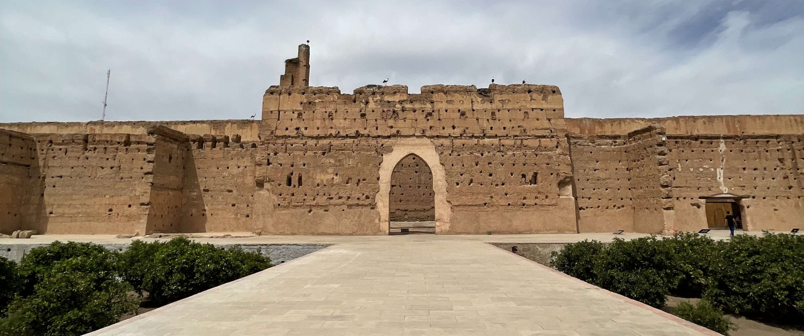 Large historic fortress wall with a central arched gate at the end of a broad stone walkway.