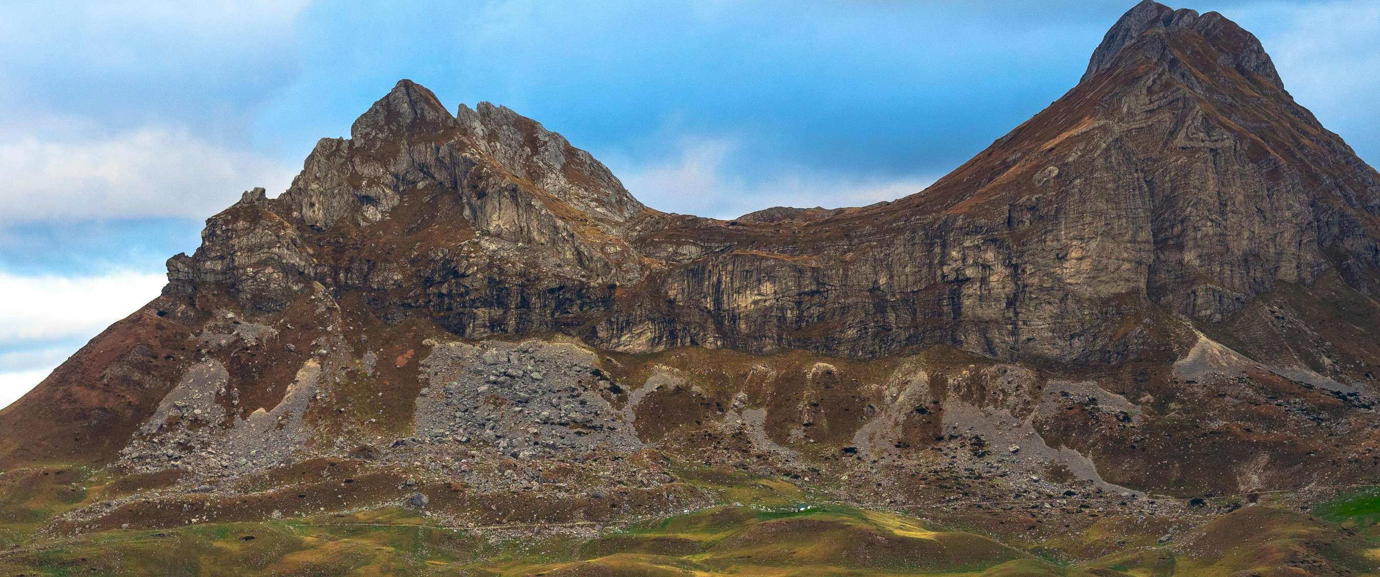 Chaîne de montagnes rocheuses avec sommets escarpés et pentes dénudées sous un ciel bleu.