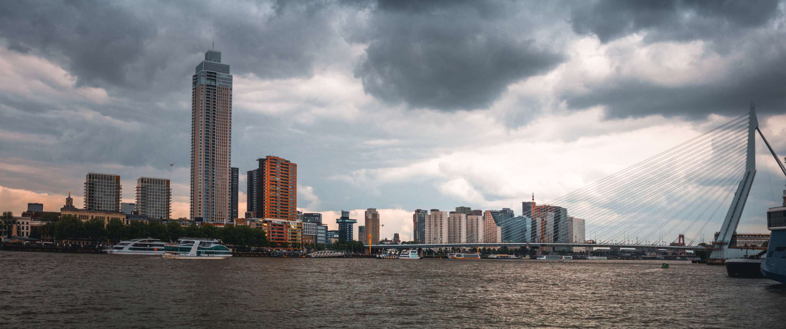 Stadsskyline aan een rivier onder donkere wolken.