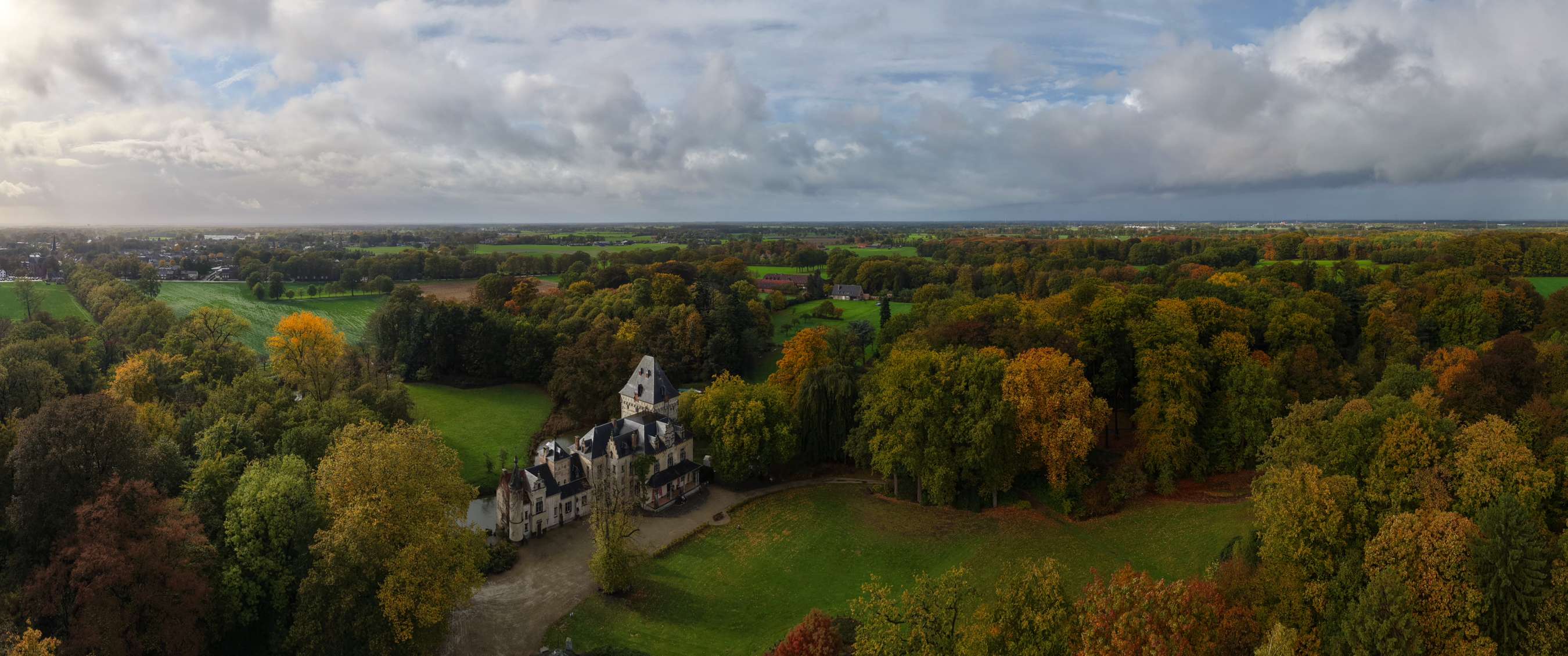 Panoramisch landschap met een historisch kasteel omringd door kleurrijke herfstbomen en open graslanden.
