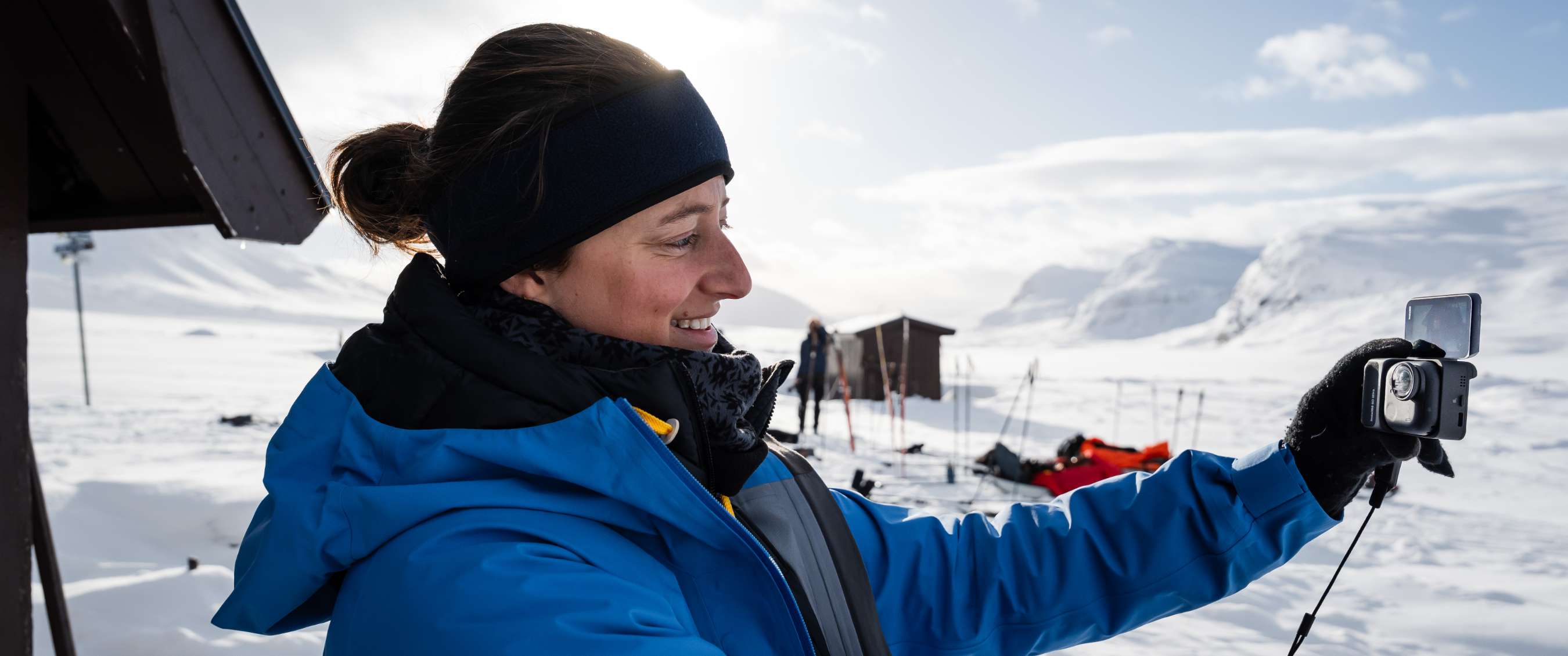 Personne en veste d’hiver bleue tenant une petite caméra dans un paysage enneigé