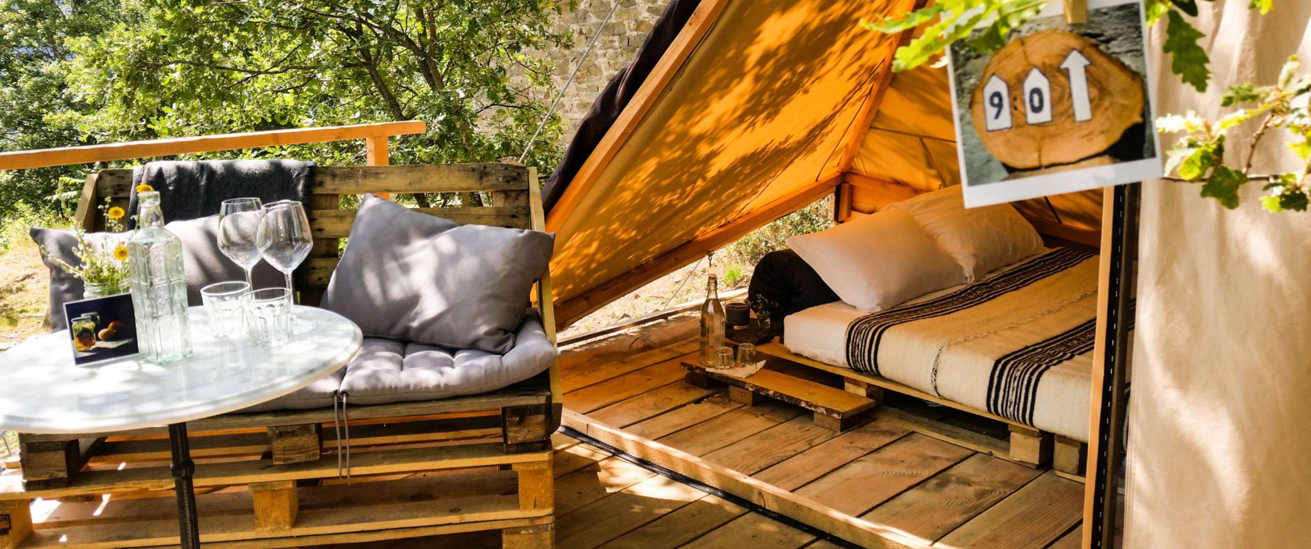 Twee beelden: buitenzitplek met tafel, glazen en kussens in een groene omgeving; interieur van een glampingtent met tweepersoonsbed en houten vloer.
