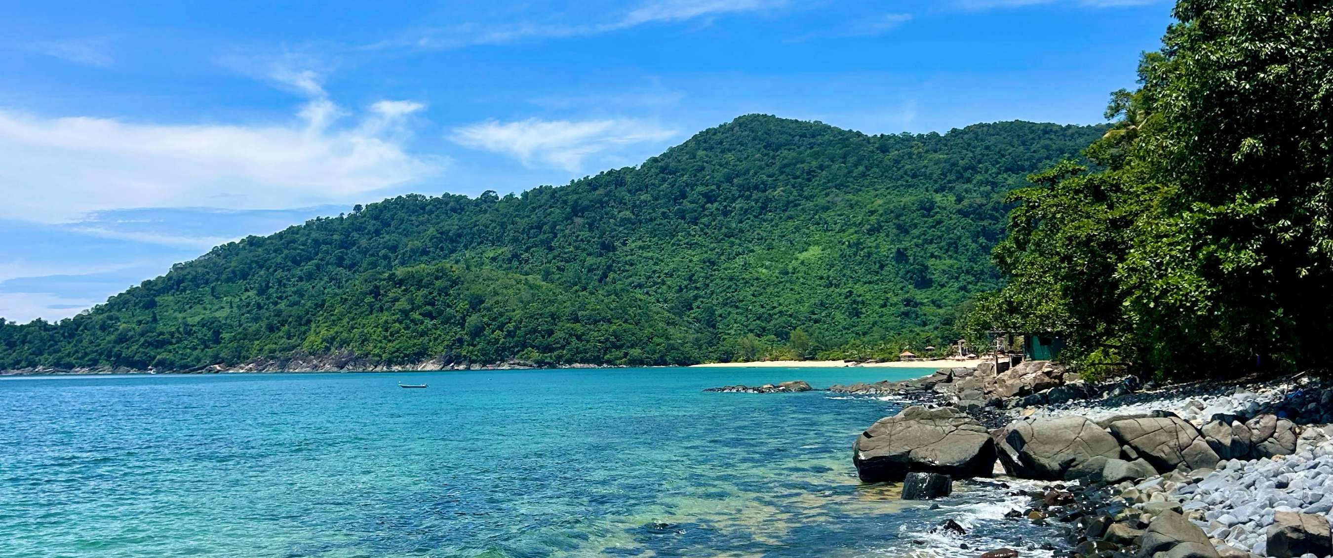 Côte tropicale avec eau bleu clair, rochers, plage et collines verdoyantes