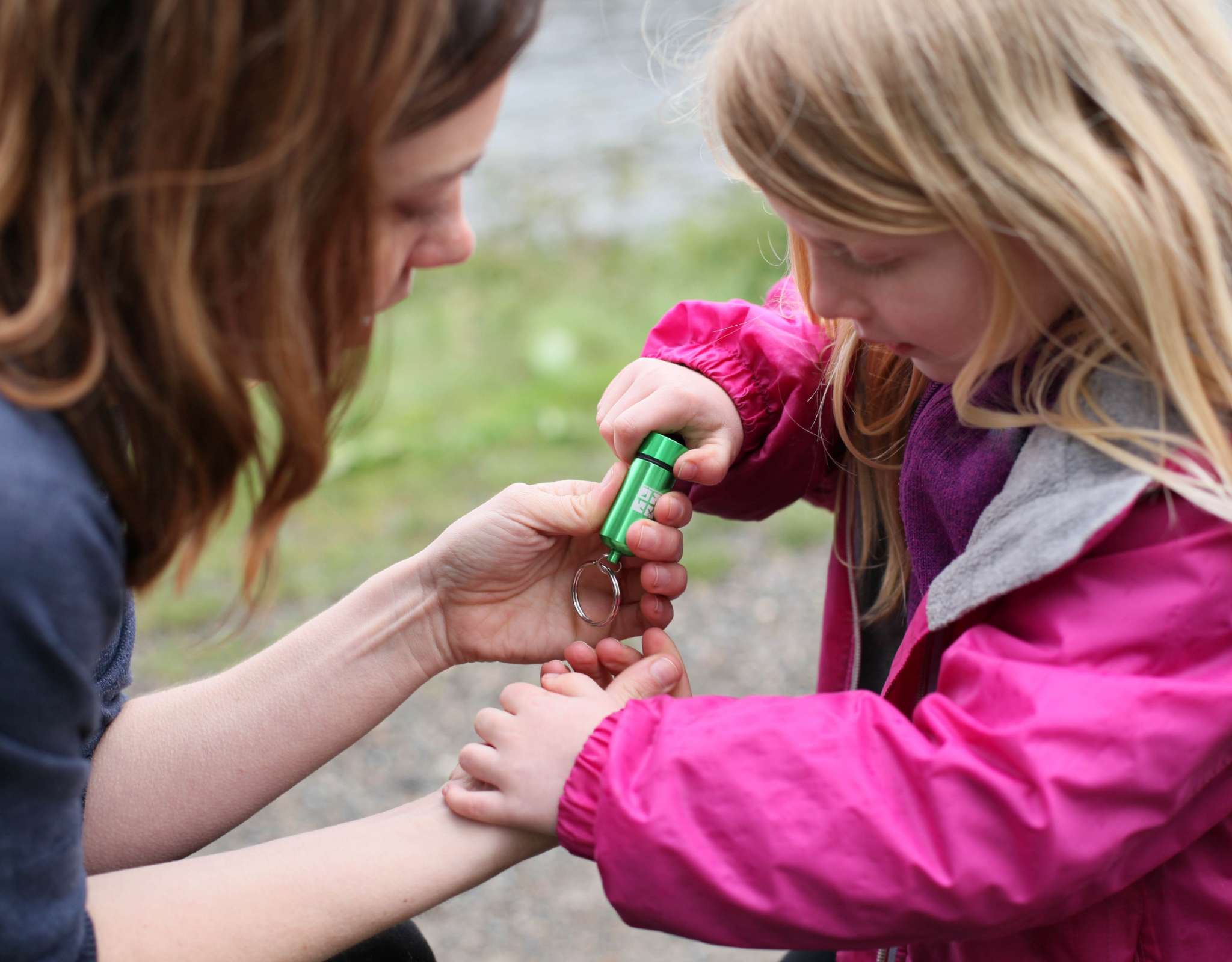 Enfant et adulte ouvrent un tube de géocache vert en extérieur