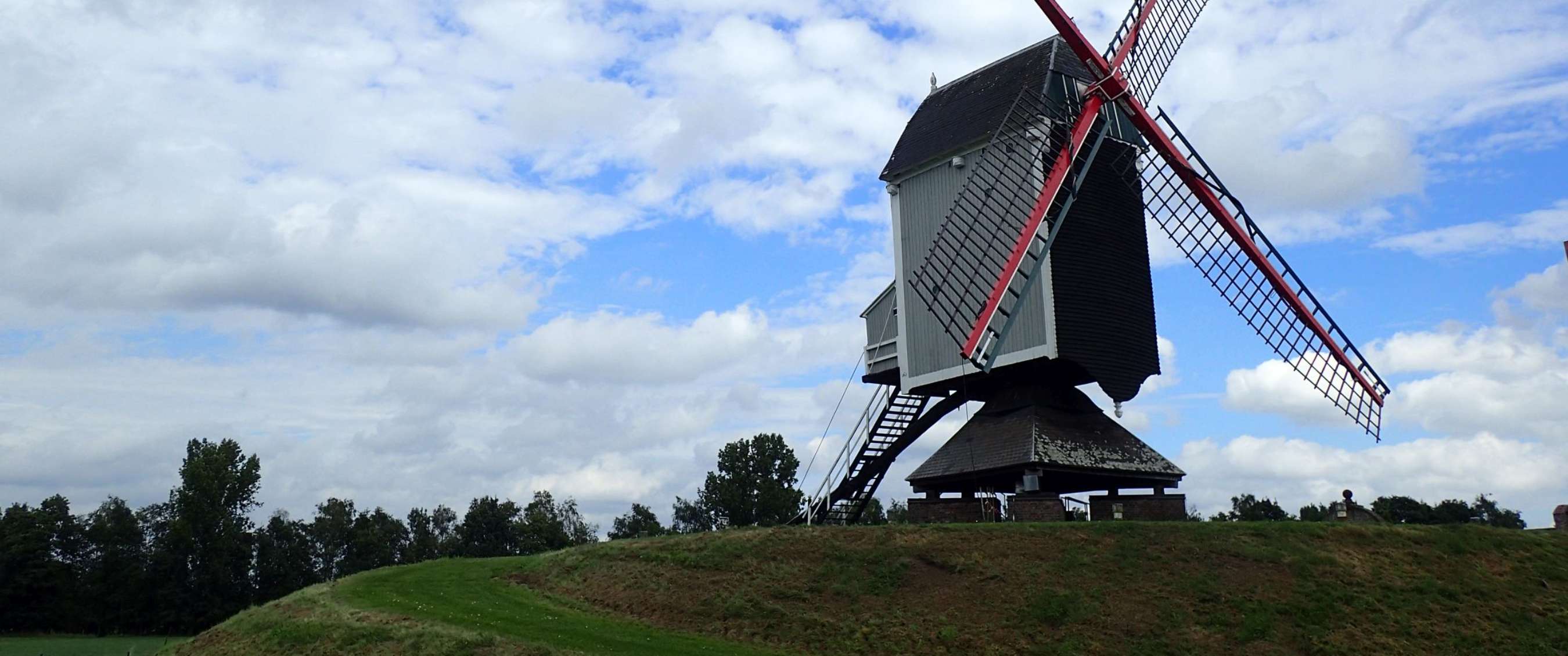 Traditionele windmolen op een groene heuvel onder een deels bewolkte lucht.