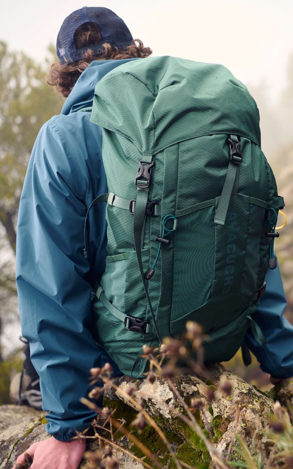 Randonneur avec grand sac vert assis sur des rochers pendant qu’une autre personne se tient sur le sentier.