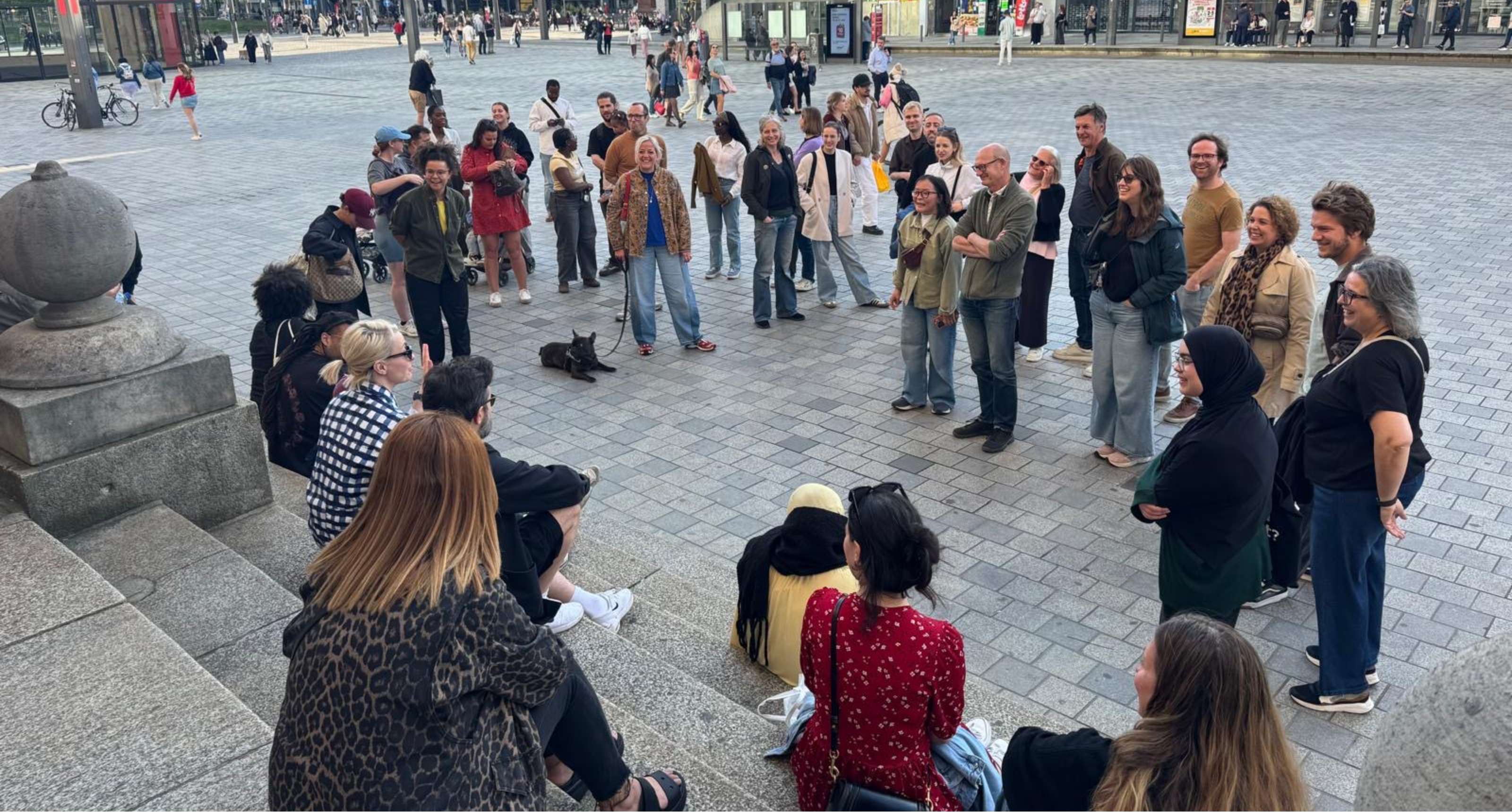 Een groep wandelaars verzamelt op een stadsplein bij een brede stenen trap.