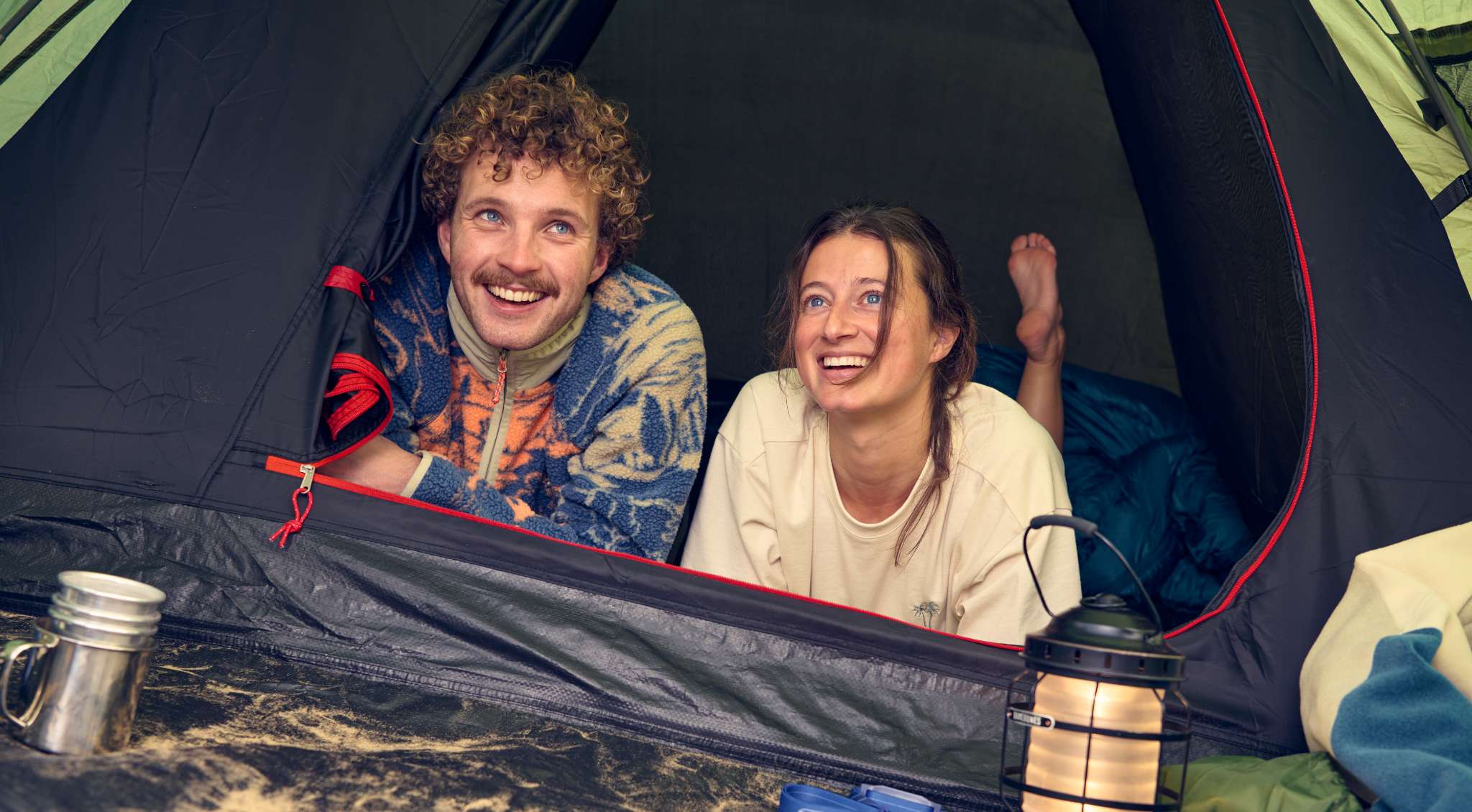 Twee kampeerders liggen glimlachend in de opening van een tent